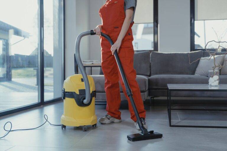 Woman in orange overall using a vacuum cleaner.