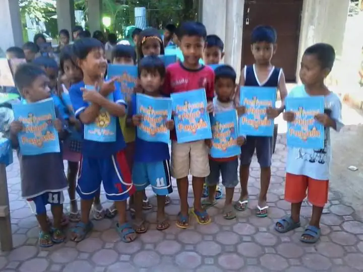 A bunch of kids cheerfully holding signs and have a big smiles on their faces.